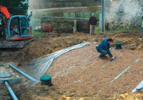 Photo d'un chantier de canalisation en travaux avec un tracteur et 2 agents entrain de recouvrir le sol de terre
