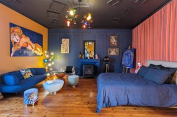 Chambre artistique de couleur bleue et jaune contenant un lit, un canapé, une table basse et des tableaux sur les murs.