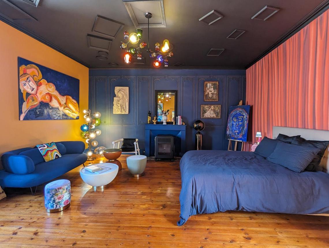 Chambre artistique de couleur bleue et jaune contenant un lit, un canapé, une table basse et des tableaux sur les murs.