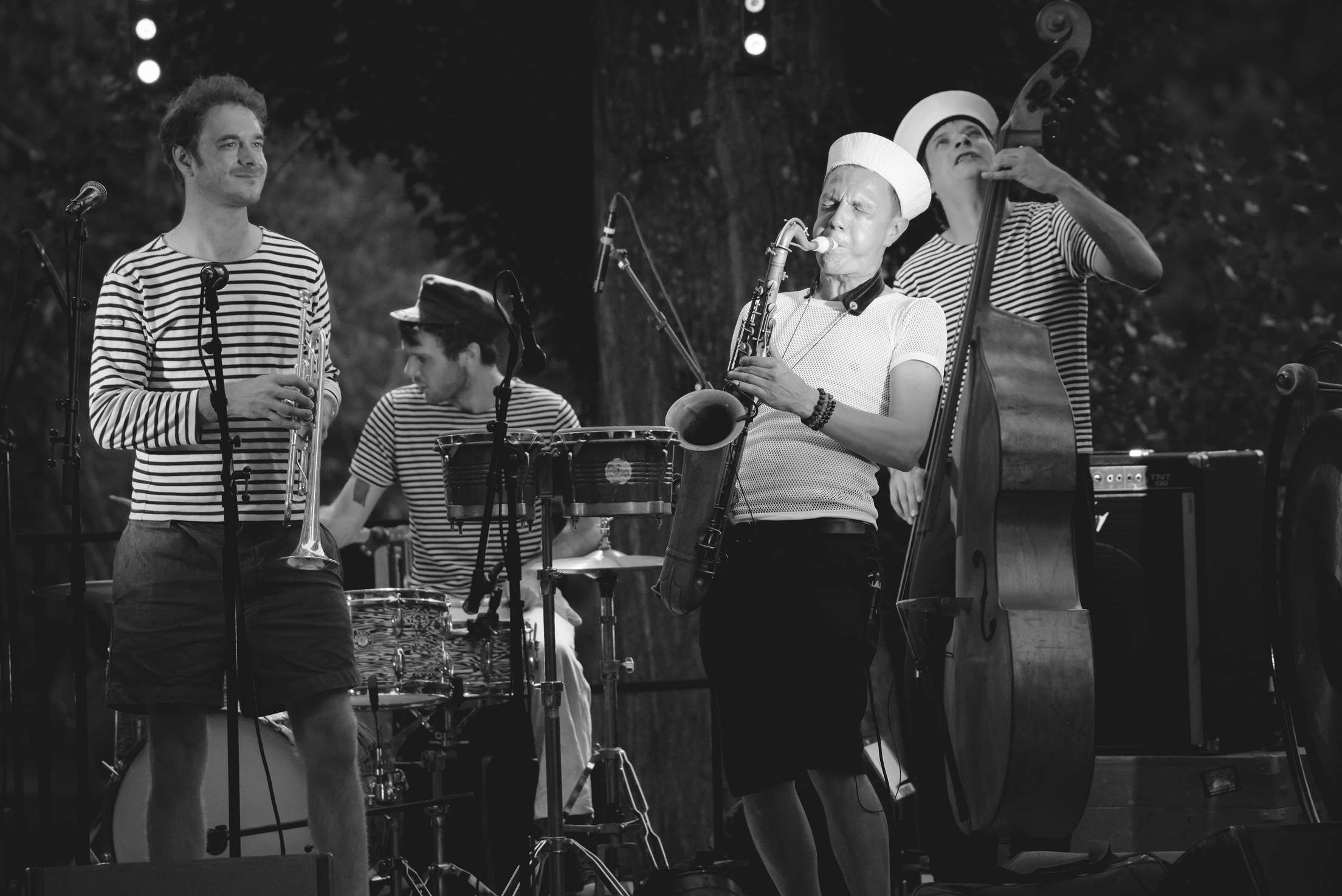 Un groupe de musique jazz sur scène, déguisé en matelot, jouent du saxophone, de la trompette, de la batterie et de la contrebasse.